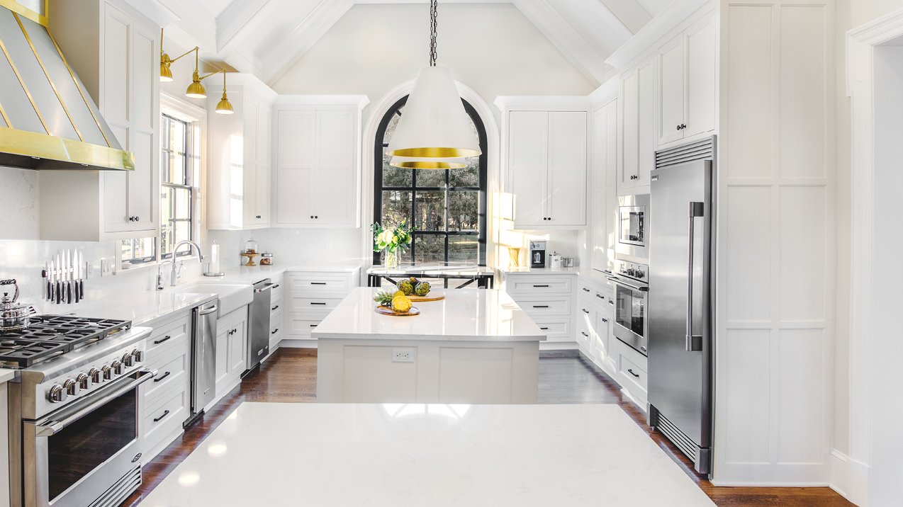 a french countryside inspired kitchen with two islands, white quartz countertops, white cabinets, and gold and black accents throughout.