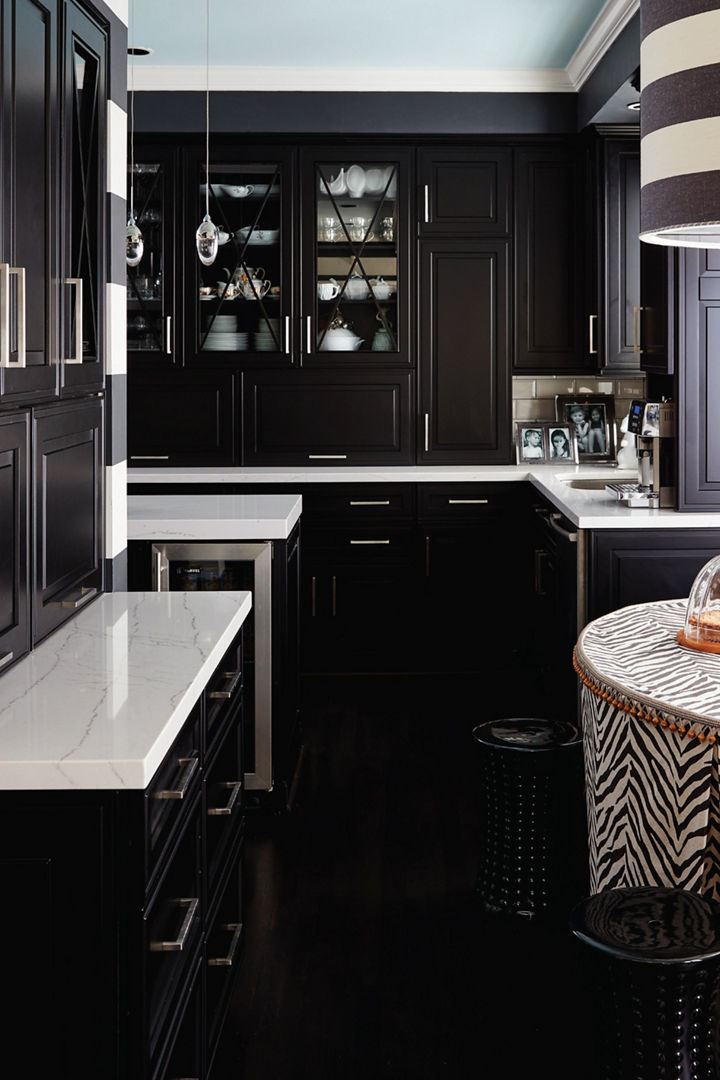 a dark and sleek modern kitchen with black cabinets, white quartz countertops, a dining table with a zebra pattern table cloth and a striped chandelier above it.