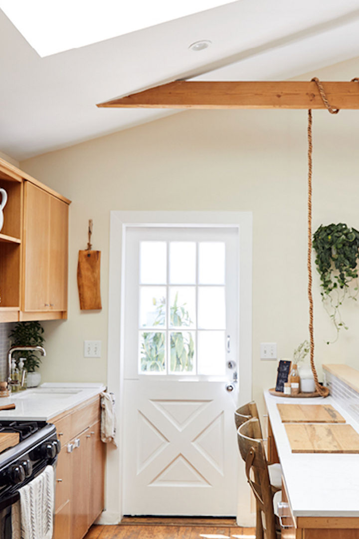 a galley kitchen with oak cabinets, white quartz countertops, wooden beams and vaulted ceilings, a farmhouse-style door leading to a patio, and an island with 2 bar stools