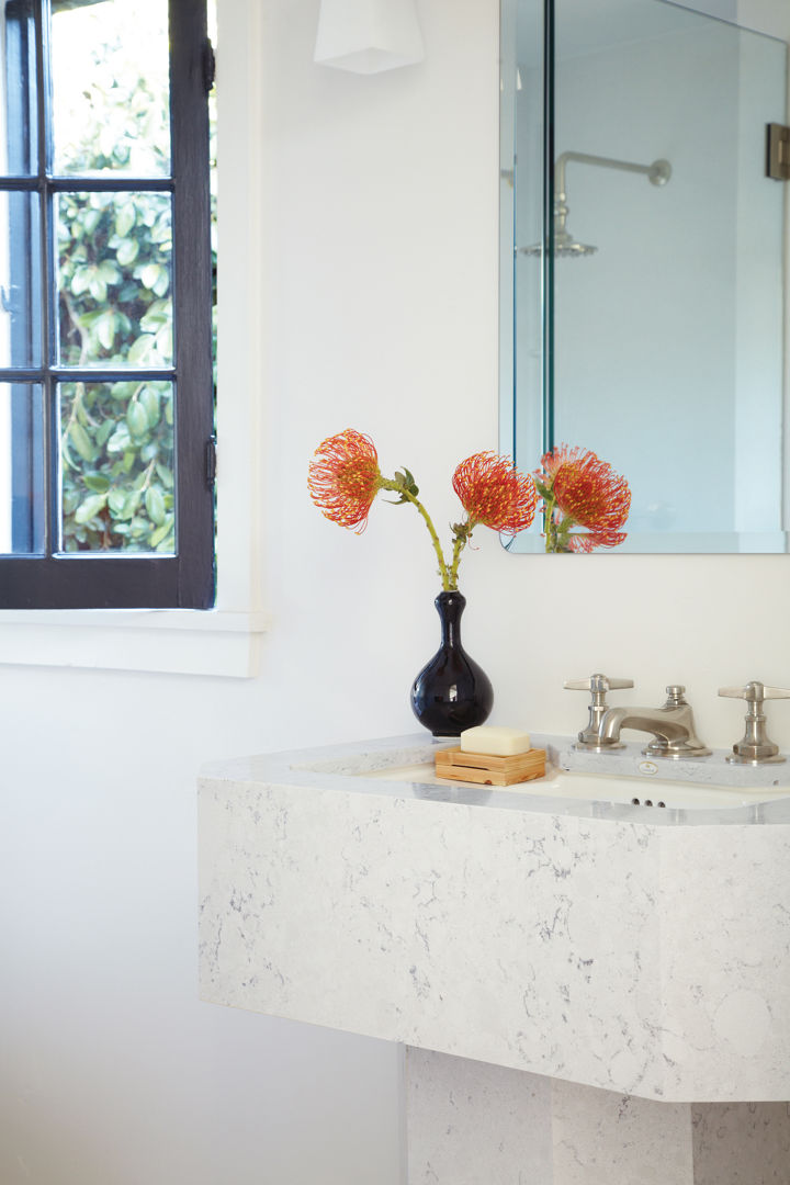 A gorgeous pedestal sink with a black window, clean mirror, and vase of flowers. 