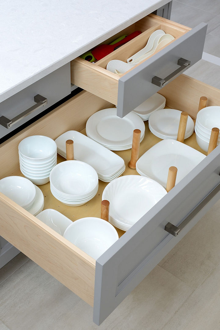 A drawer with plates stored inside gray cabinetry beside a Cambria Weybourne quartz countertop.