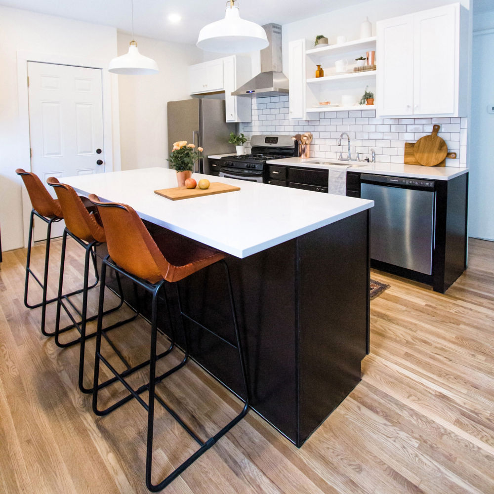 A kitchen with black lower cabinets, white upper cabinets, open shelving, modern appliances, and a center island topped with white quartz countertops.