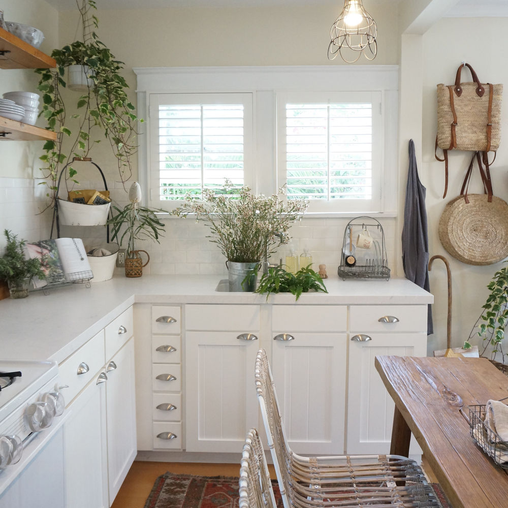 small, vintage looking kitchen with white cabinets, open shelving, two small windows, overhead lighting, and a center table made from wood.