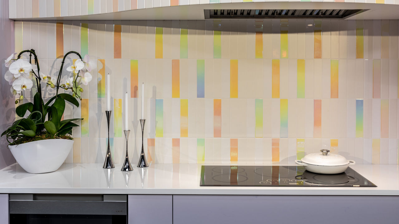 A unique candy-colored backsplash in a kitchen with purple cabinets and white quartz countertops.