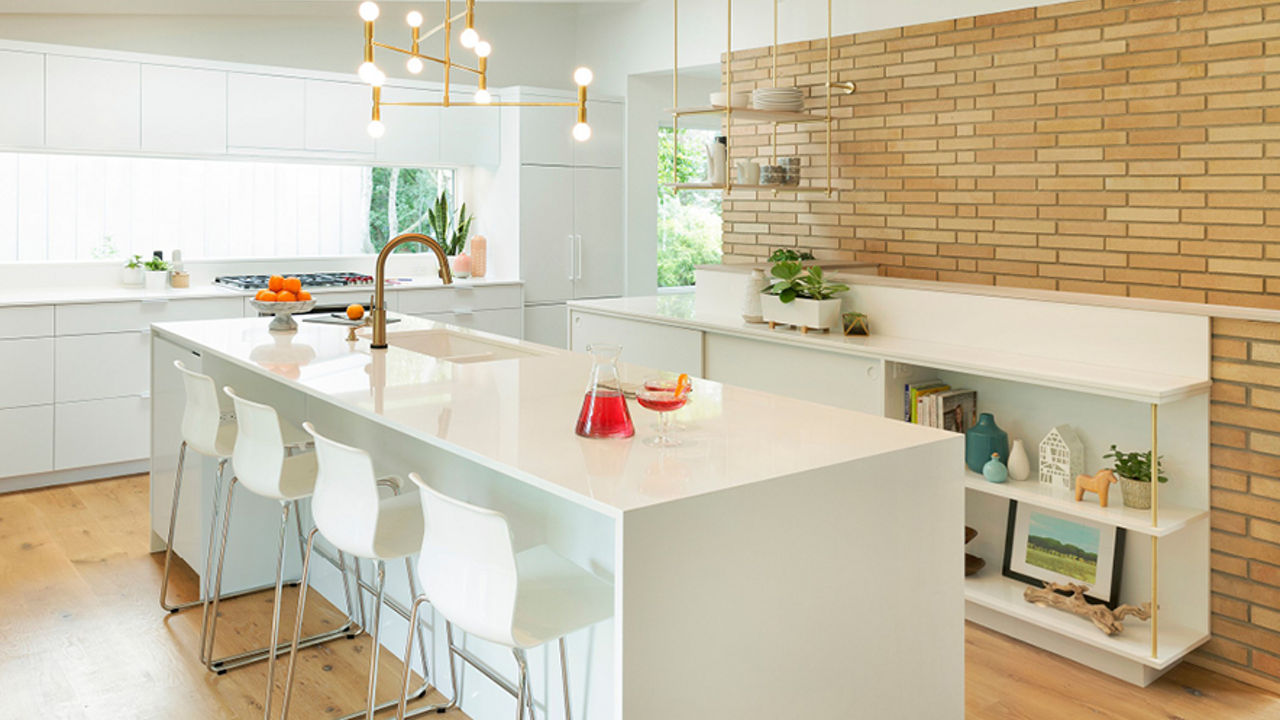 A clean white kitchen featuring a tan brick wall, open shelving, a big window, and white quartz kitchen island made from Cambria White Cliff.