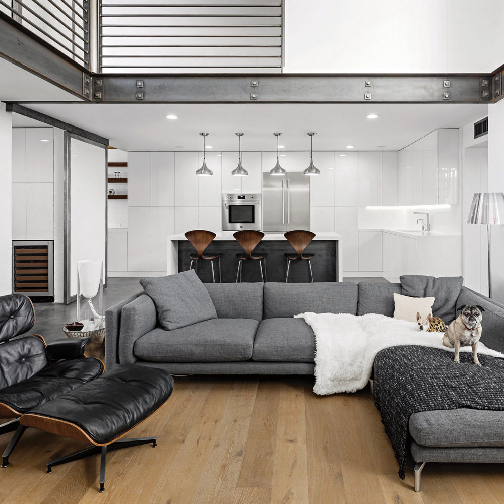 A contemporary living room with a gray couch, black leather chair, wooden flooring, and raised ceilings. 