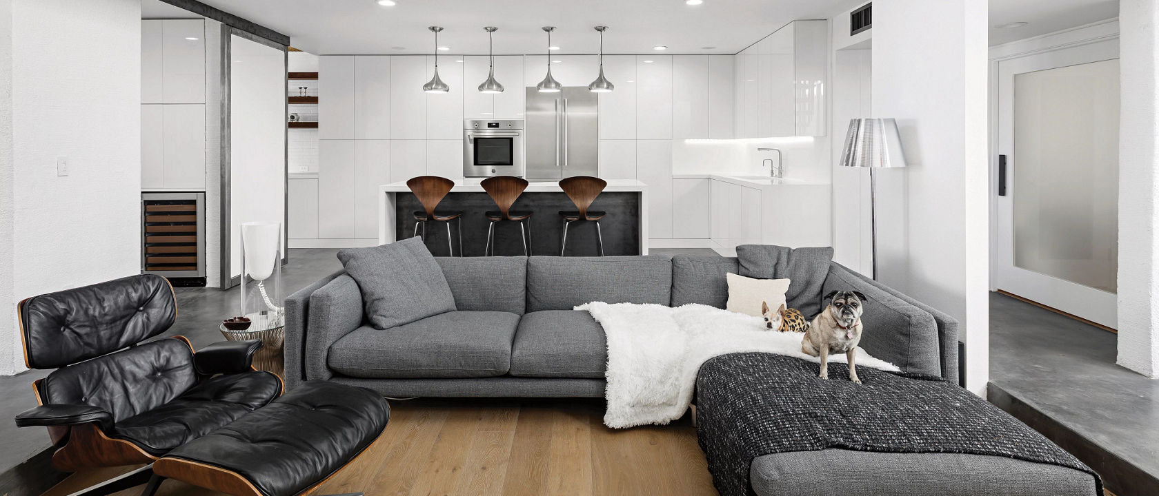 A contemporary living room with a gray couch, black leather chair, wooden flooring, and raised ceilings. 