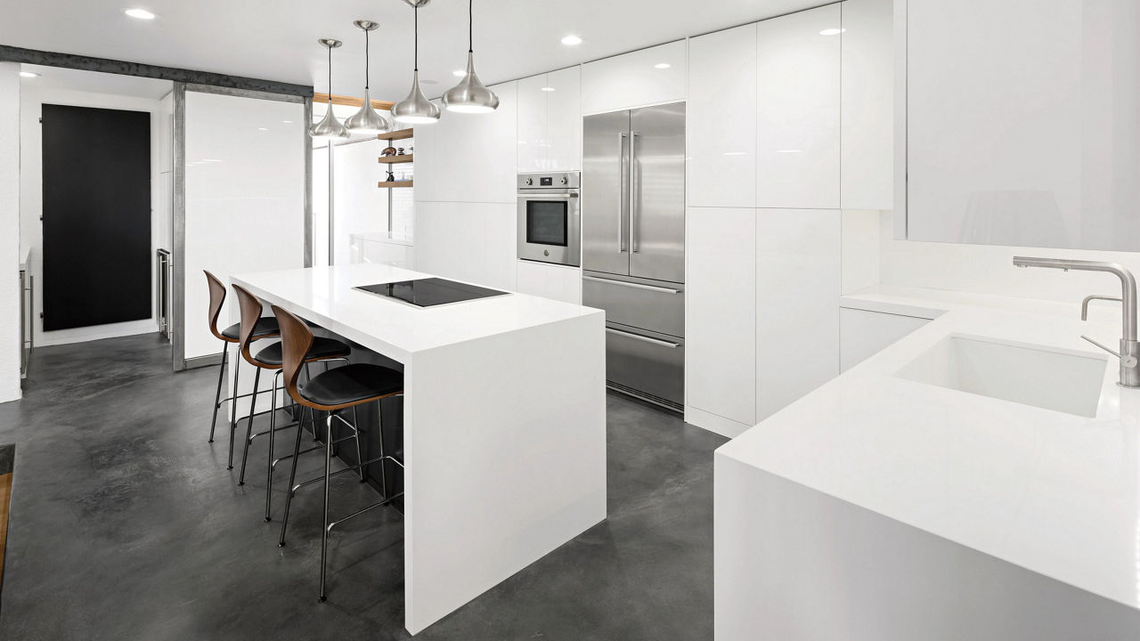 A modern kitchen with white cabinets, white quartz double island waterfall, black flooring, and stainless-steel appliances.