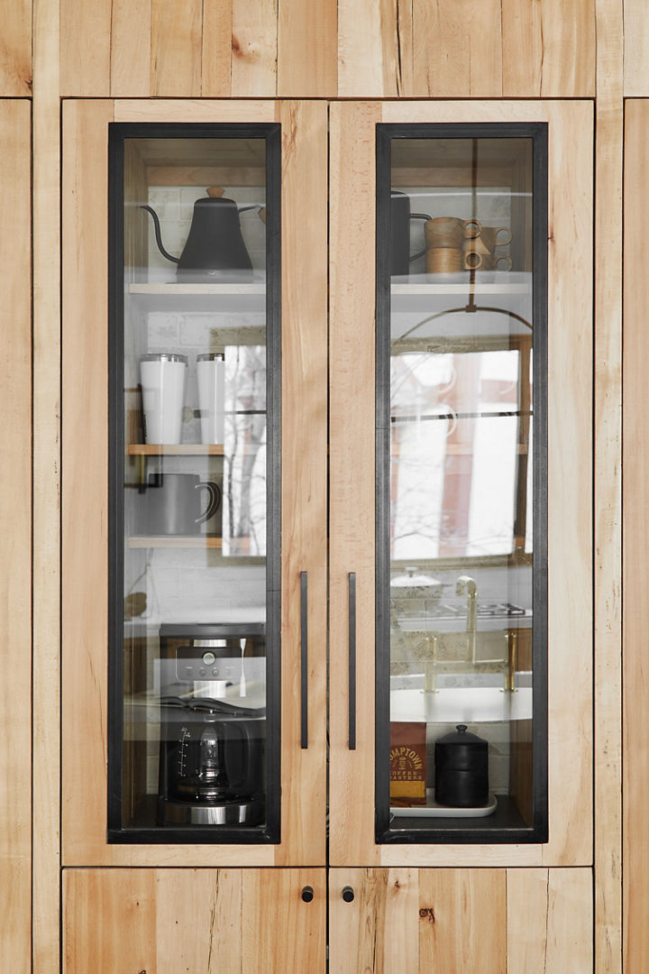 A vertical wooden cabinet with glass revealing coffee pots and tea kettles inside the cabinet.