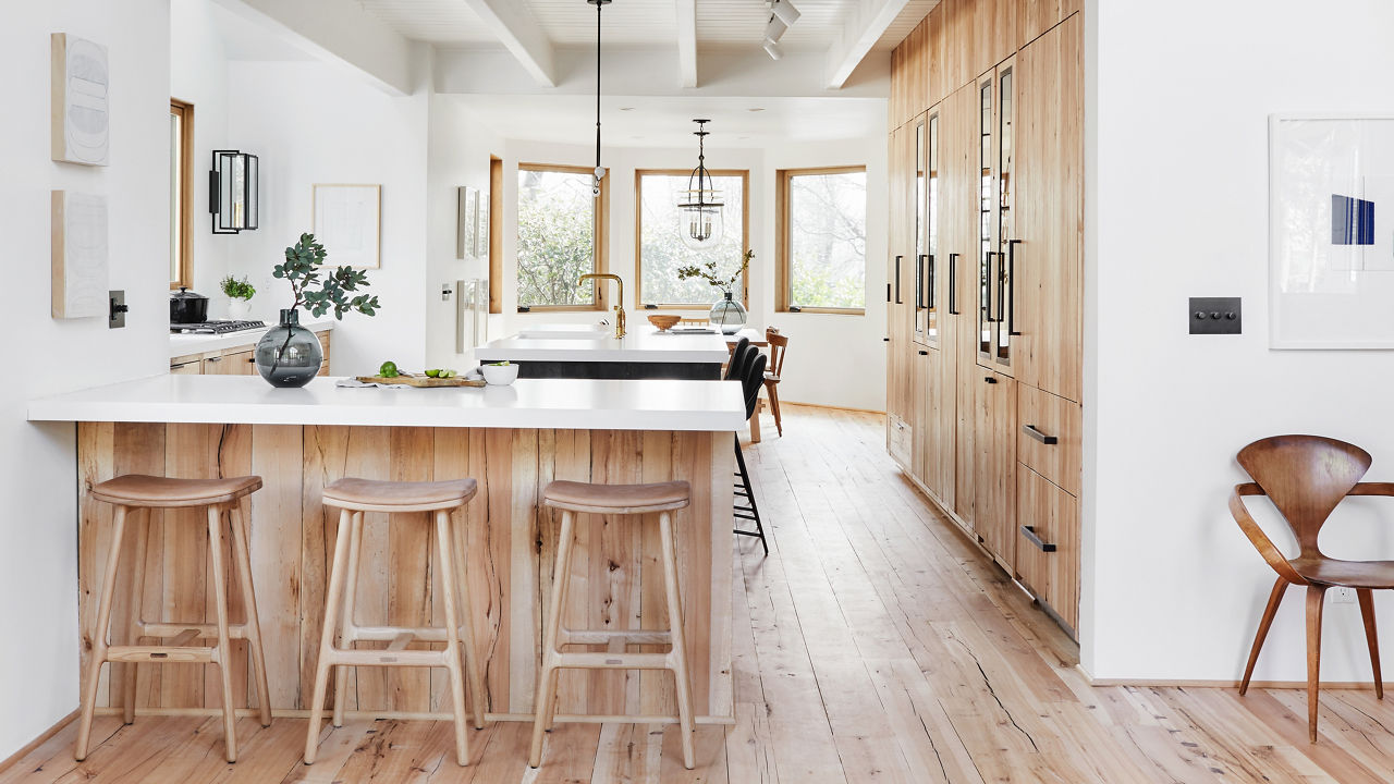 a mountain house kitchen with white walls, white quartz countertops, gorgeous oak stained cabinets, three matching bar stools, and floor-to-ceiling cabinets.