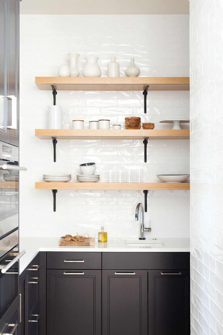 a butler's pantry with white subway tile, black cabinets, white quartz countertops, and open shelving.
