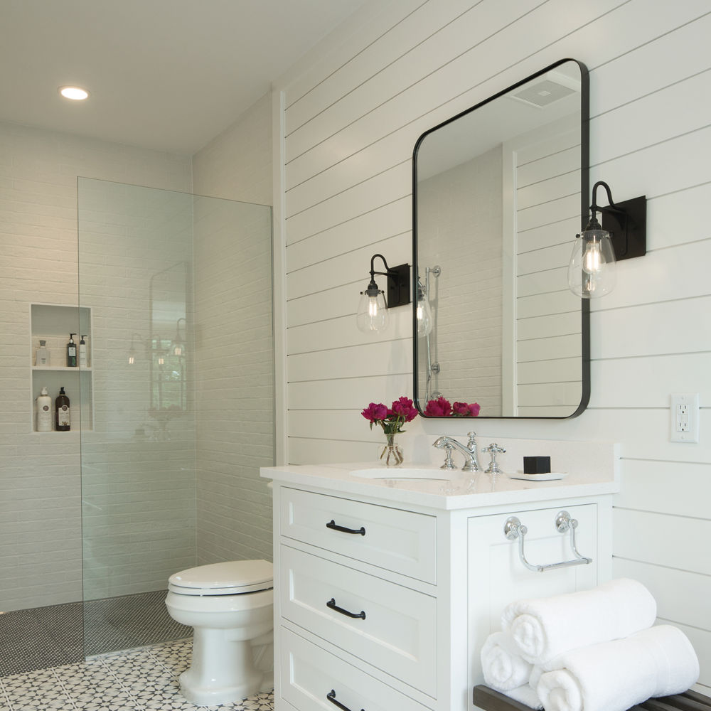 A coastal bathroom with a white vanity topped with white quartz, shiplap walls, a black mirror and lights, and a gorgeous walk-in shower.