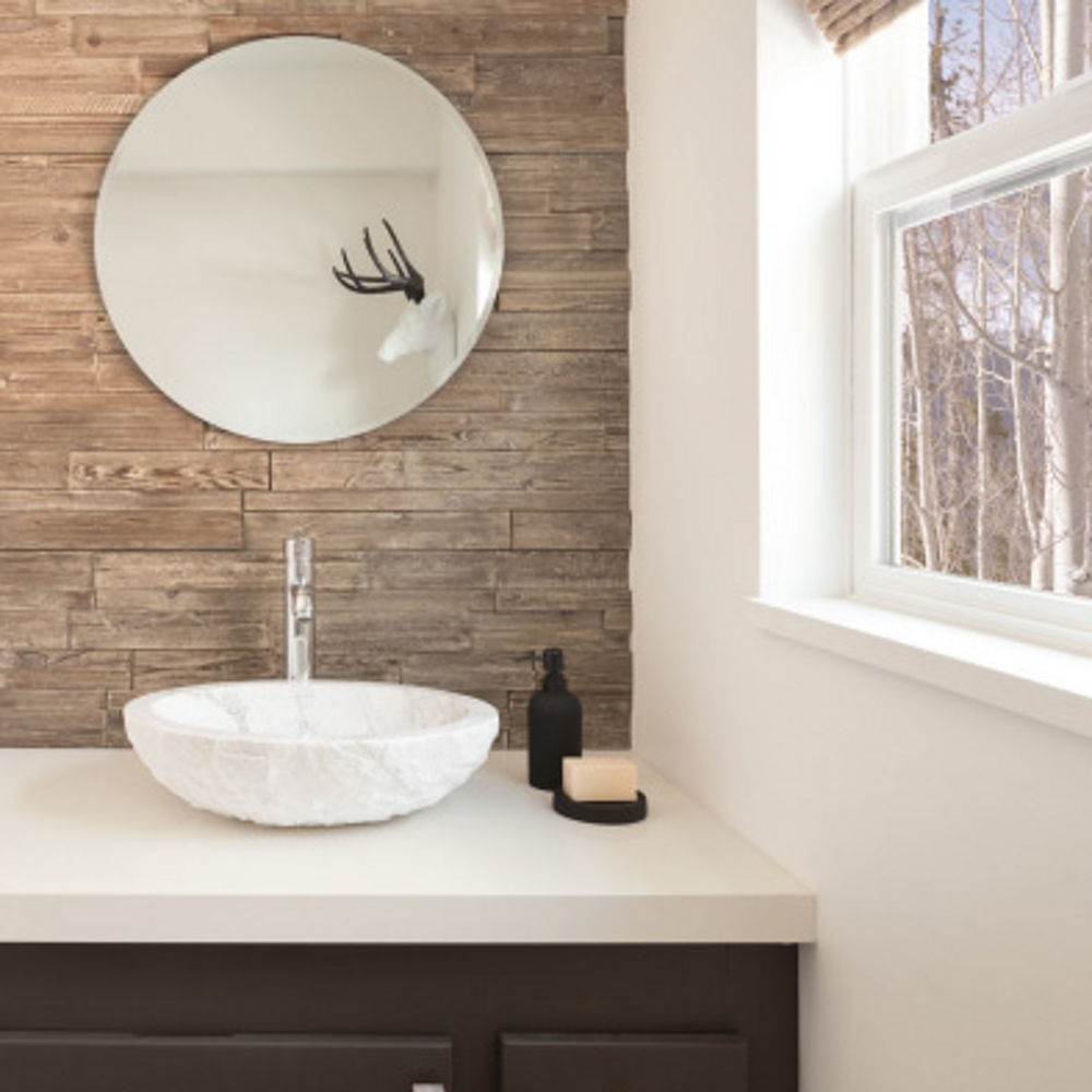a bathroom with a dark brown vanity topped with white quartz countertops, a circular mirror, and a wooden wall behind.