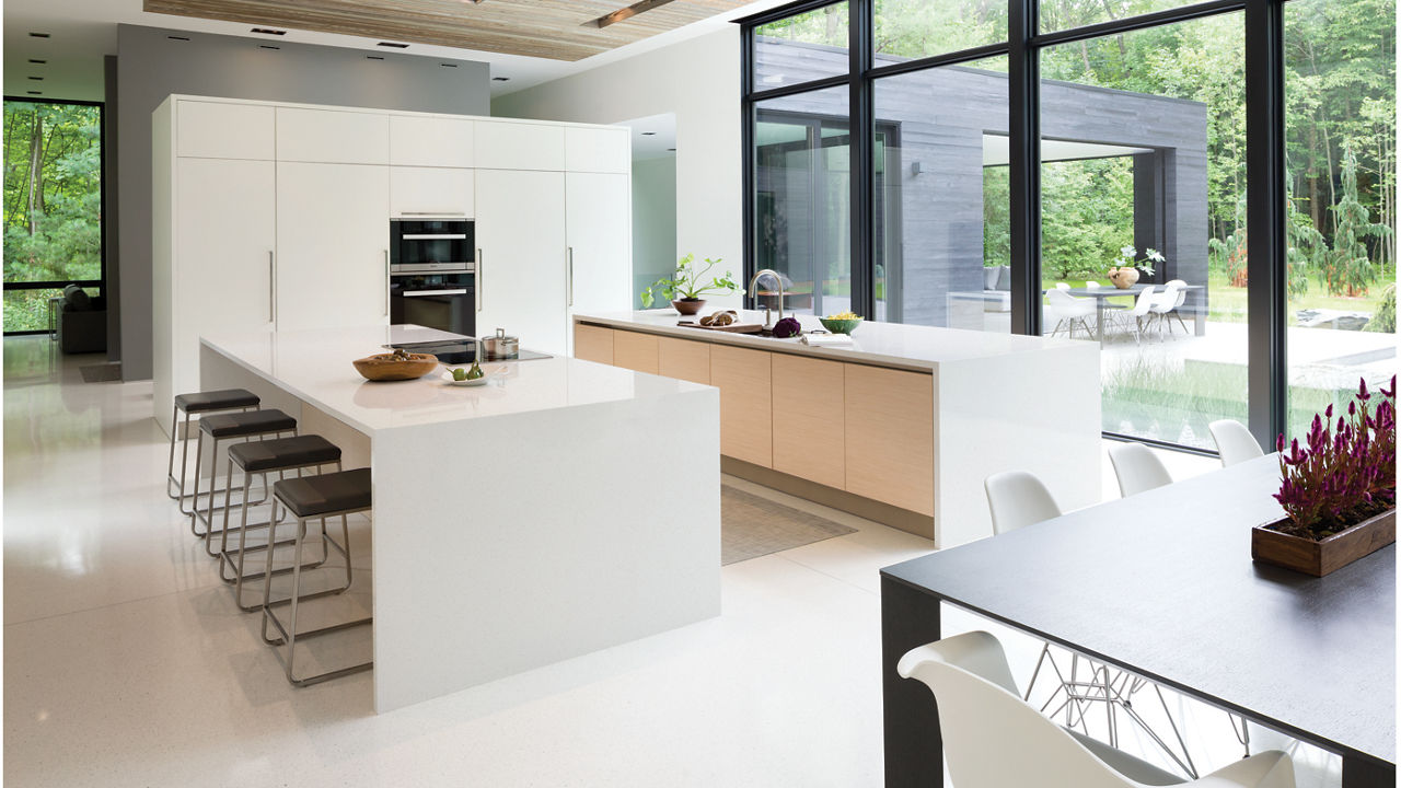 A modern, clean kitchen with two double waterfall edge island topped with white quartz with a gorgeous view of a lush forest.