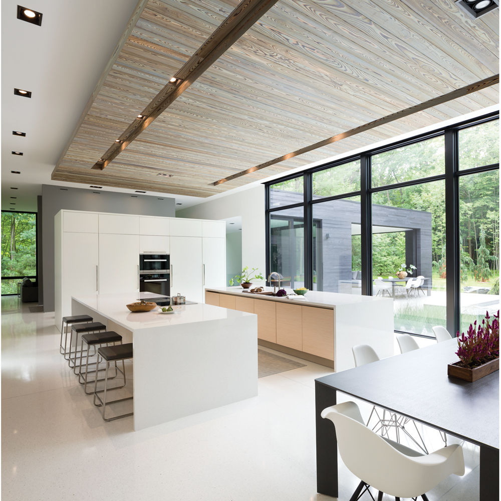 A modern, clean kitchen with two double waterfall edge island topped with white quartz with a gorgeous view of a lush forest.