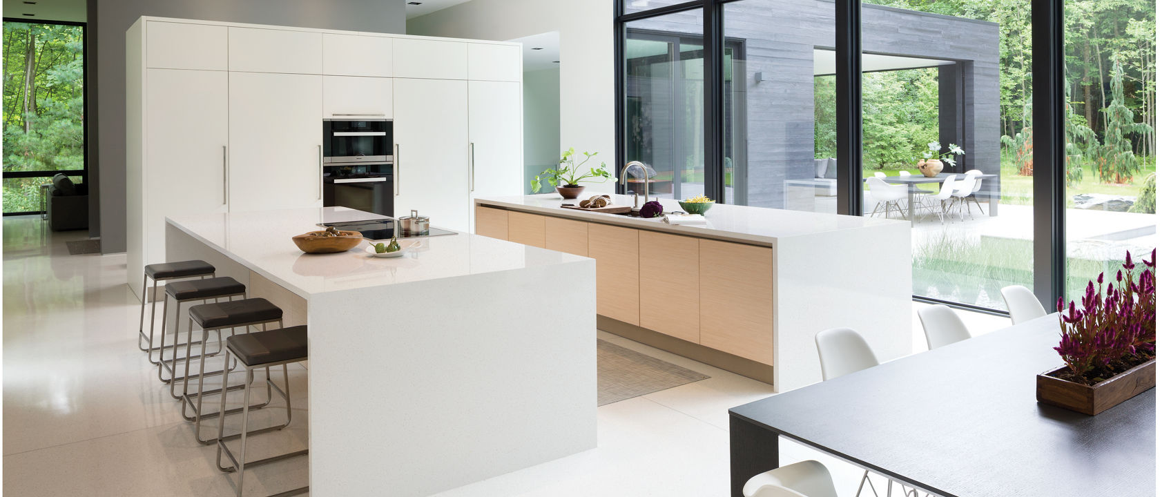 A modern, clean kitchen with two double waterfall edge island topped with white quartz with a gorgeous view of a lush forest.