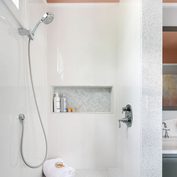 A shower made from white quartz with a shower seat, light green wall and floor tiles, and orange walls.