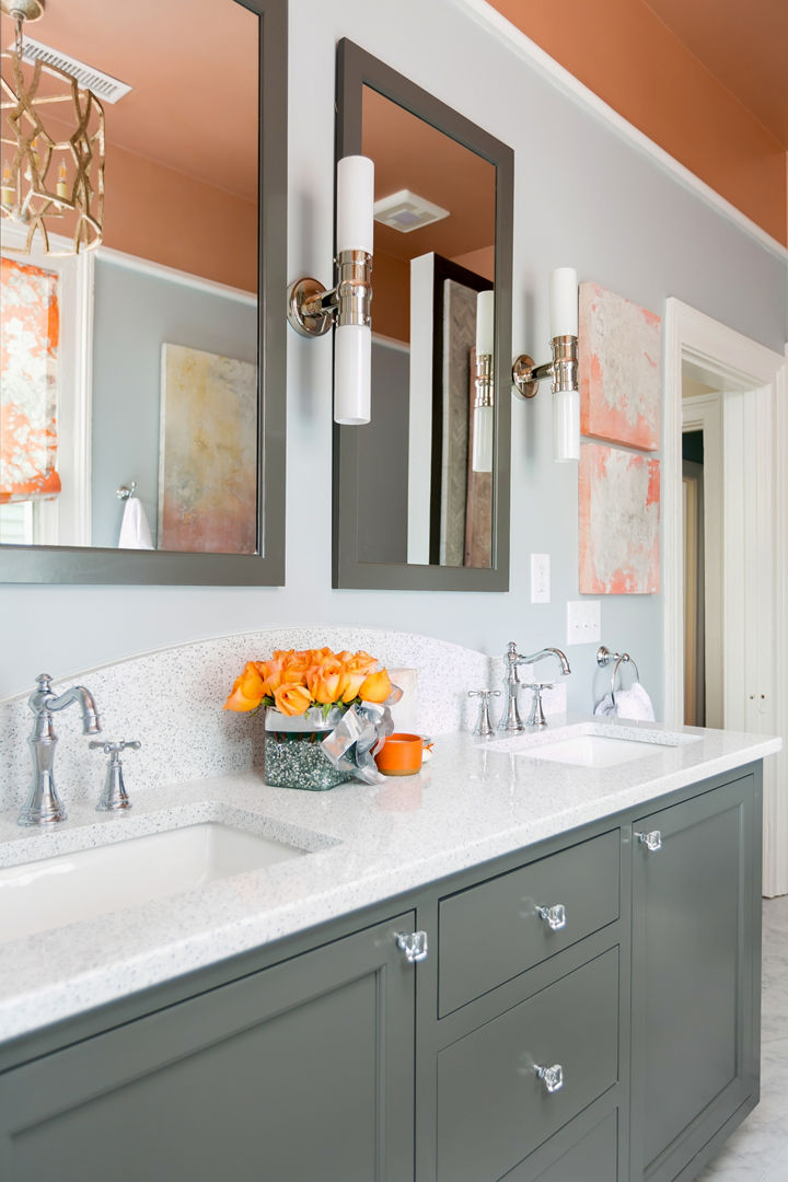 A farmhouse style bathroom with an olive green vanity, white quartz countertops, a double sink with two mirrors and wall lighting, with orange walls and decorations