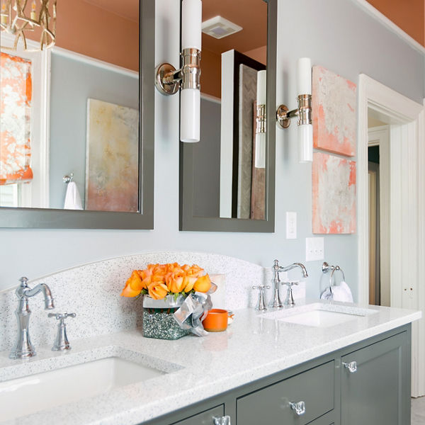A farmhouse style bathroom with an olive green vanity, white quartz countertops, a double sink with two mirrors and wall lighting, with orange walls and decorations