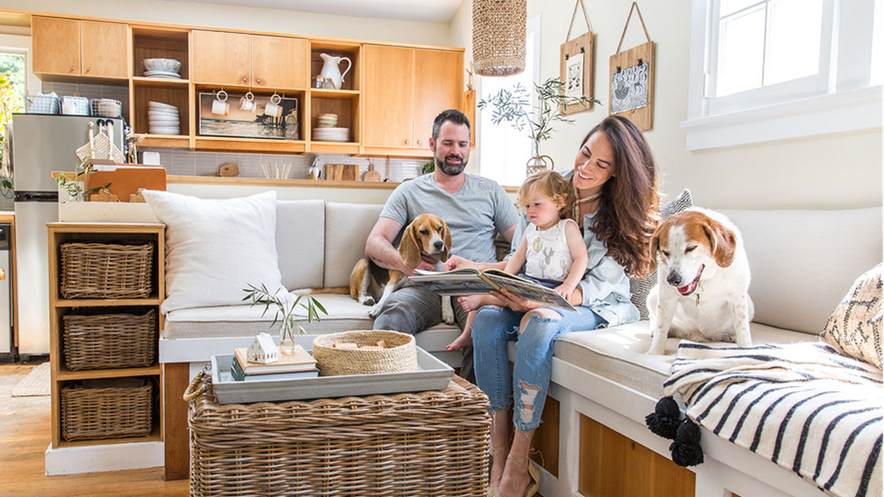 Whitney Leigh Morris and her family sitting on a white couch in a living room beside an open kitchen.
