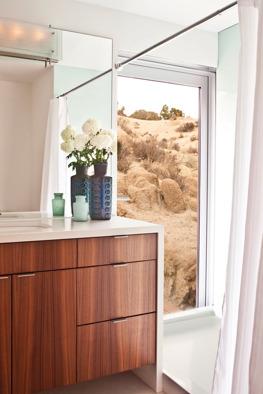 a mid-century modern vanity with a waterfall edge quartz countertop, wooden cabinets and a large shower window
