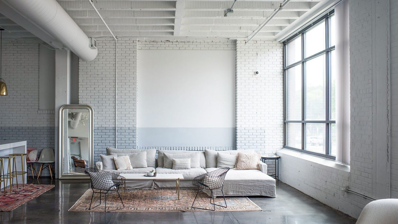 a living room with a white couch, coffee table, vintage rug, and two wicker chairs. 