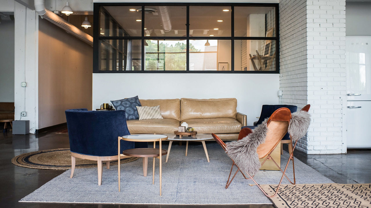 a living room with a leather couch, blue armchairs, area rug, and a circular coffee table.