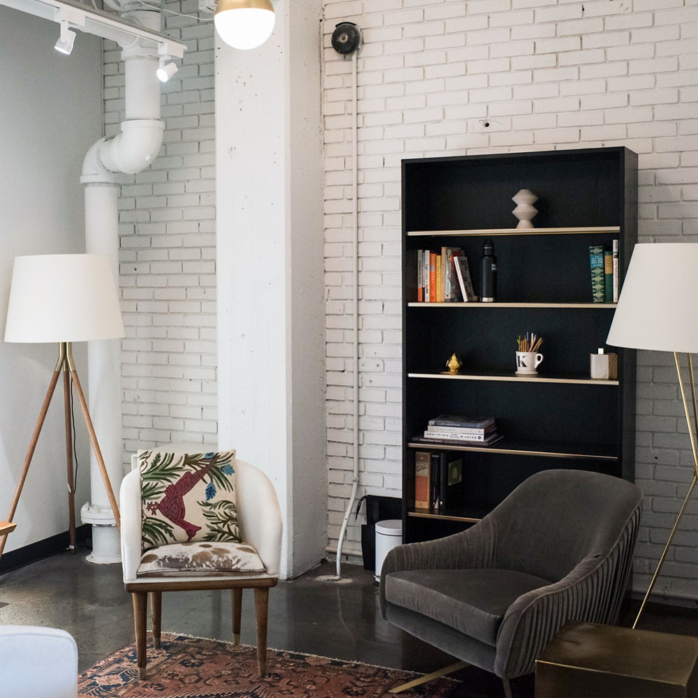 a seating area with exposed white brick, circular mirror, seating options, and a black bookshelf. 